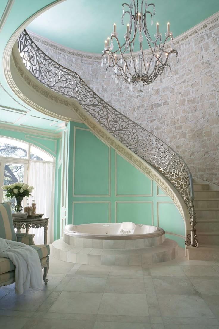 A luxurious bathroom featuring a circular bathtub, a grand staircase with an ornate railing, and a chandelier.